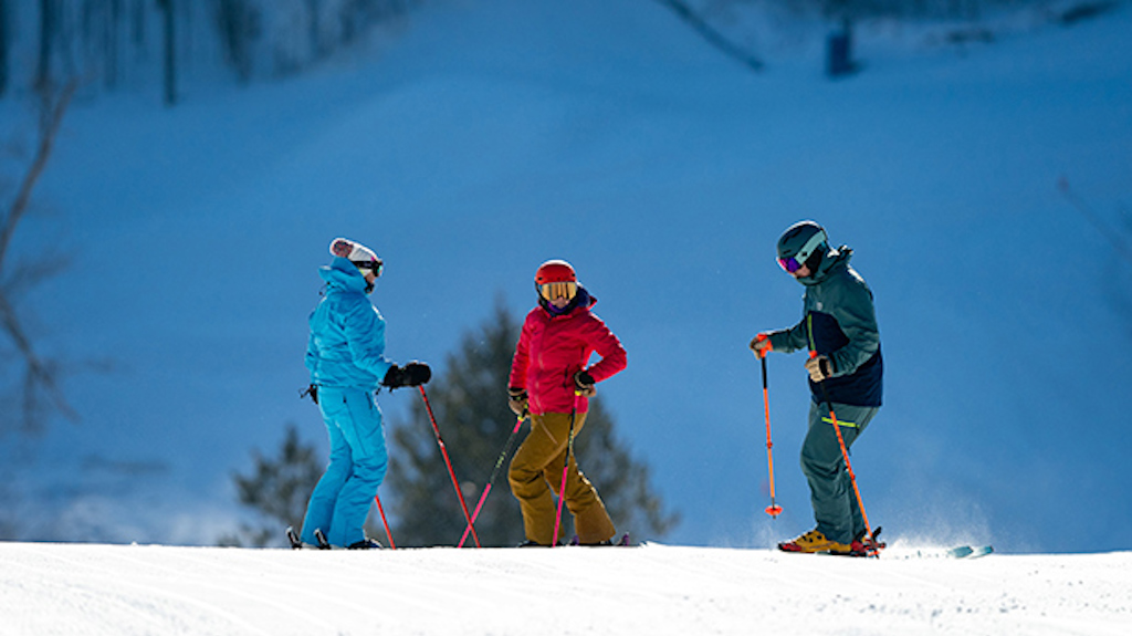 Three skiers standing on a slope talking to each other on a sunny day. 